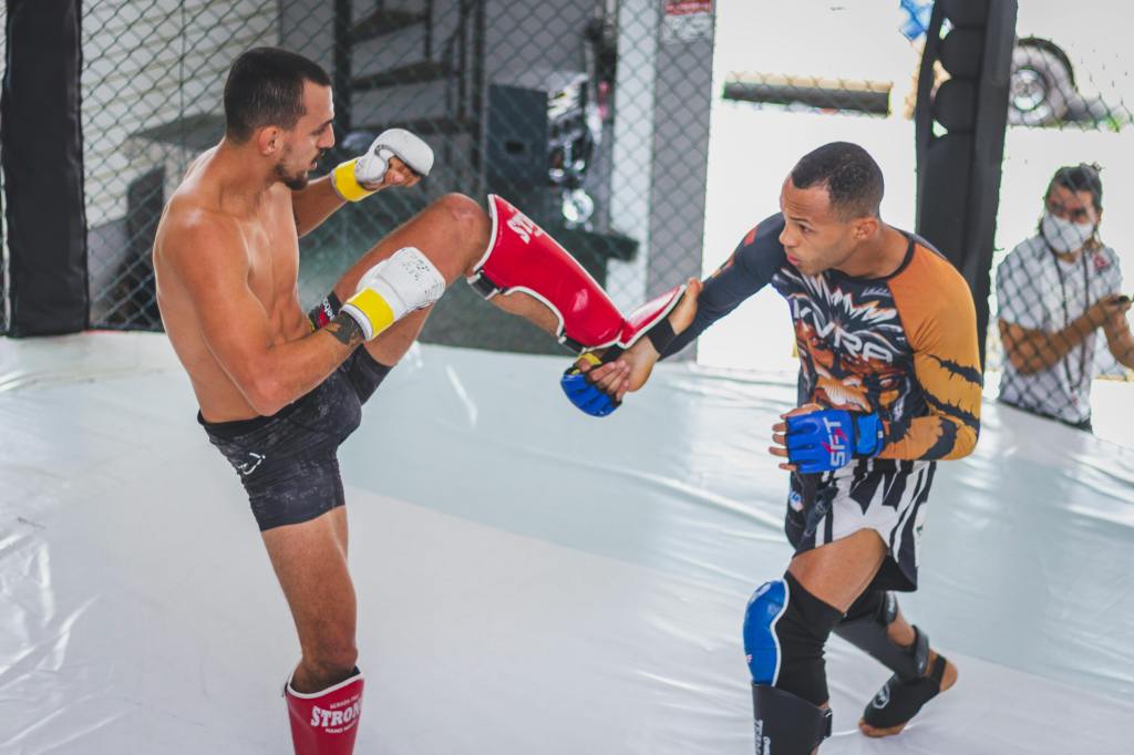 Two fighters practicing MMA techniques in a training facility, one delivering a knee strike while the other holds a focus pad.